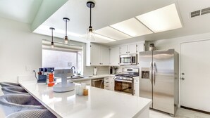 A modern kitchen with white cabinetry, stainless steel appliances, and a central island with bar stools. - Game Room, Hot Tub & Mtn Views: Palm Springs Gem (Palm Springs)