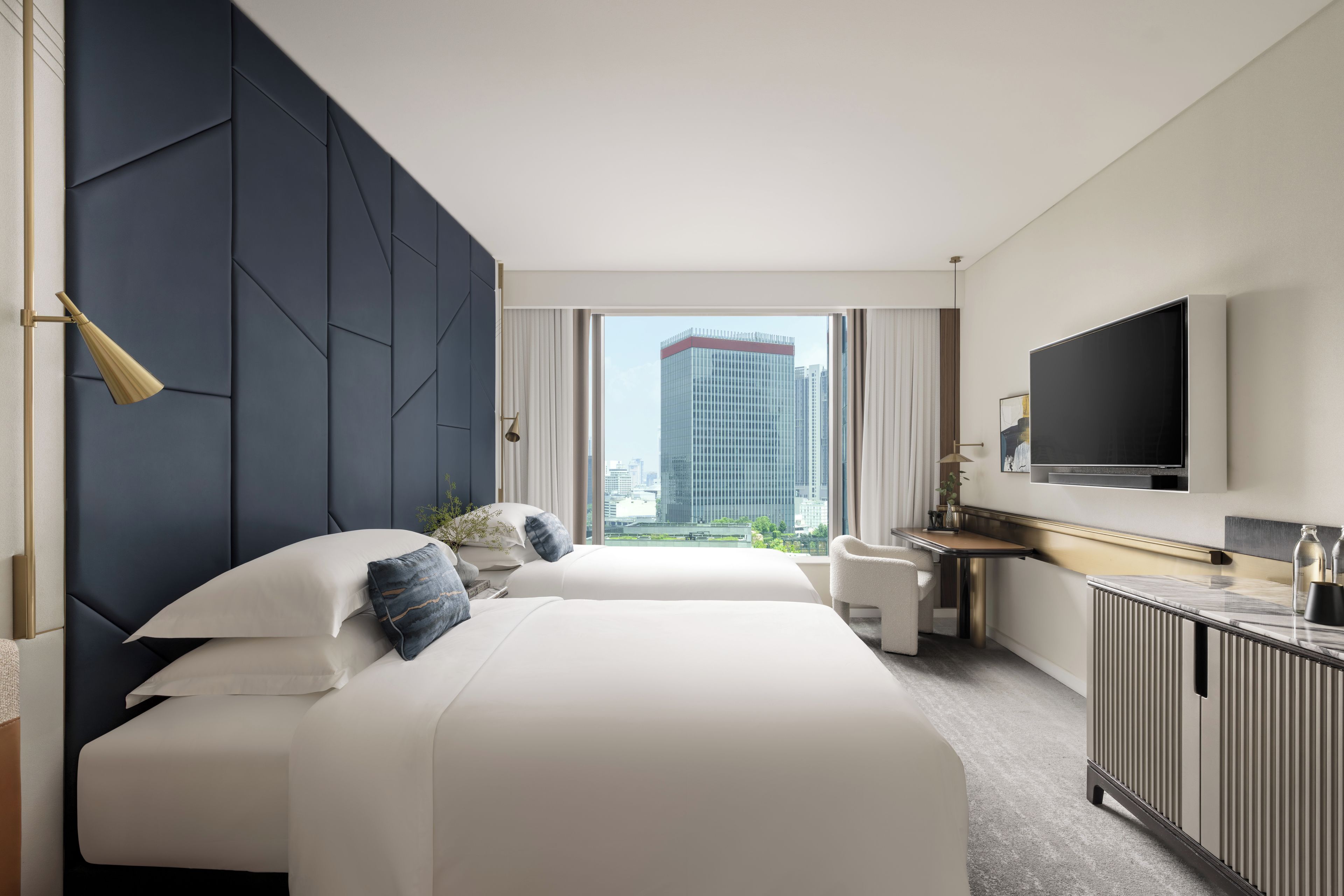 A modern hotel room with a large bed, a desk, a flat-screen TV, and a city view.