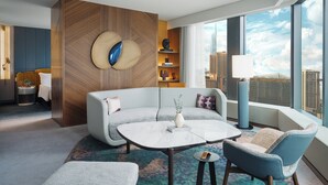 A modern hotel room with a large window, a sofa, a coffee table, and a small side table.
