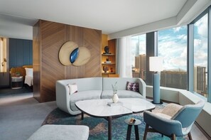 Una habitación de hotel moderna con un ventanal grande, un sofá, una mesita de centro y una mesita auxiliar.