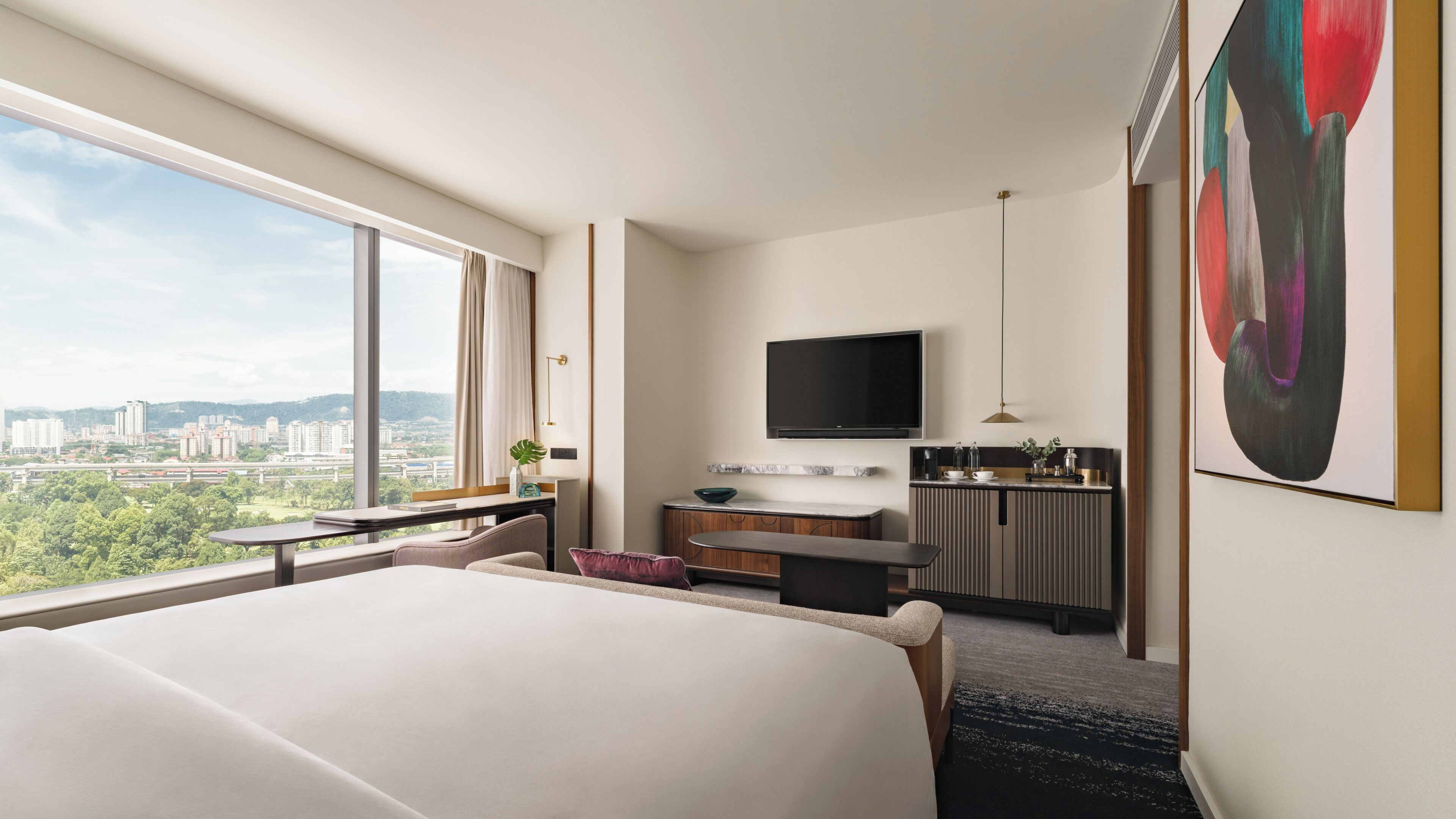 A hotel room with a large bed, a desk with a flat-screen TV, a dining area, and a city view.