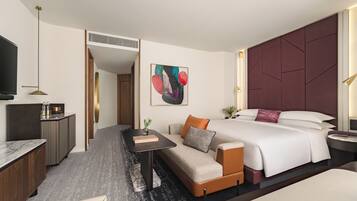 A hotel room with a bed, sofa, desk, TV, and artwork.