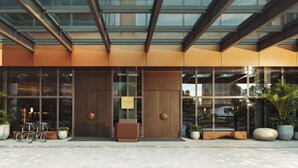 A modern building entrance with large glass windows, a wooden door, and potted plants.