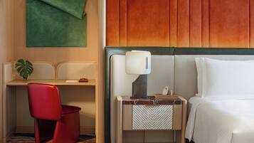 A hotel room with a bed, a desk with a chair, a nightstand with a lamp, and a green wall.