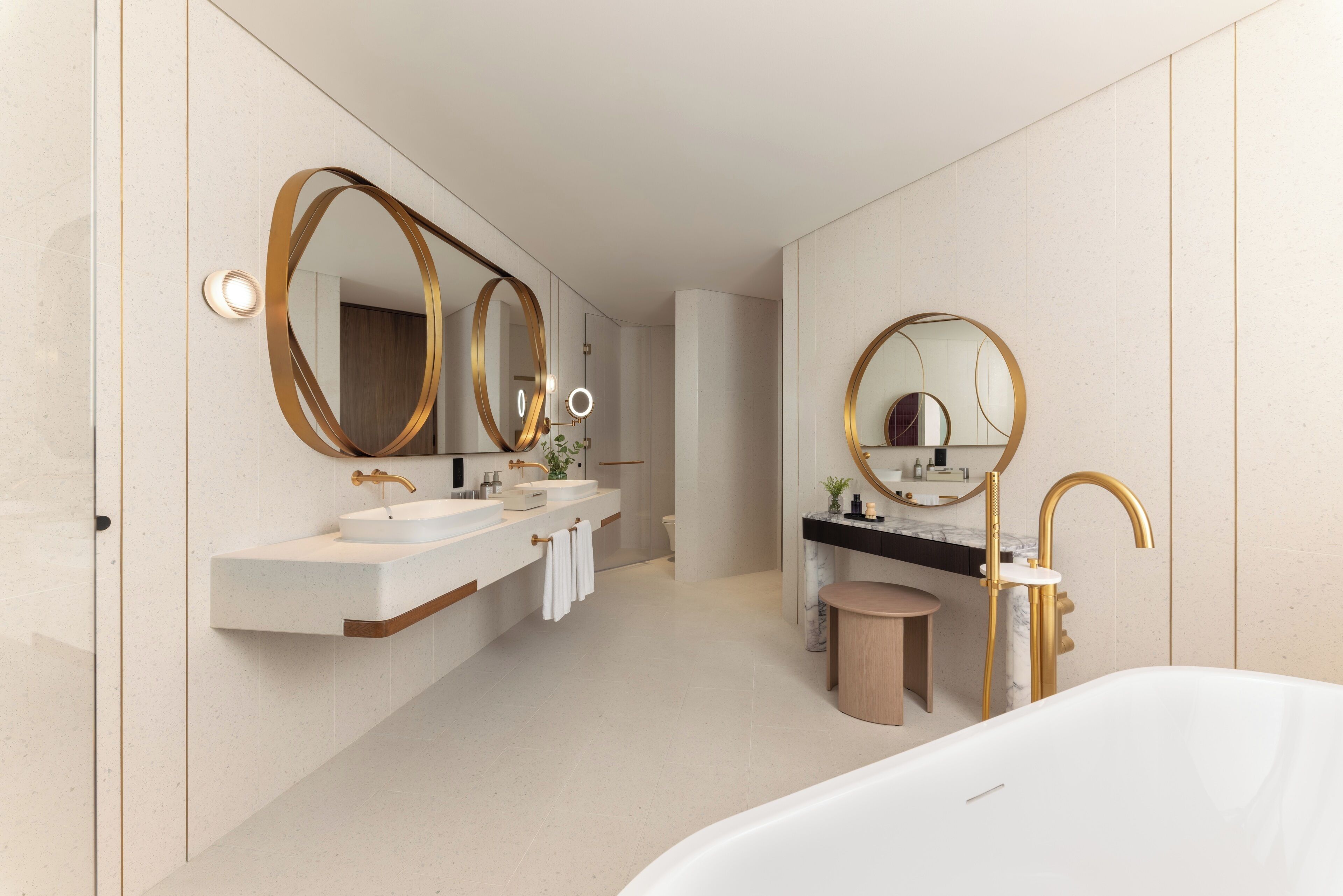 Un baño moderno con una bañera grande, un lavamanos doble y un espejo amplio con marcos dorados.