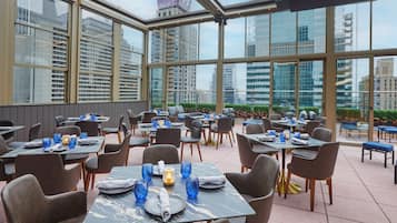 Un restaurante con mesas dispuestas para comer, ventanas amplias y vistas panorámicas de la ciudad.