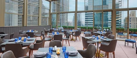 A restaurant with tables set for dining, large windows, and a view of the cityscape.
