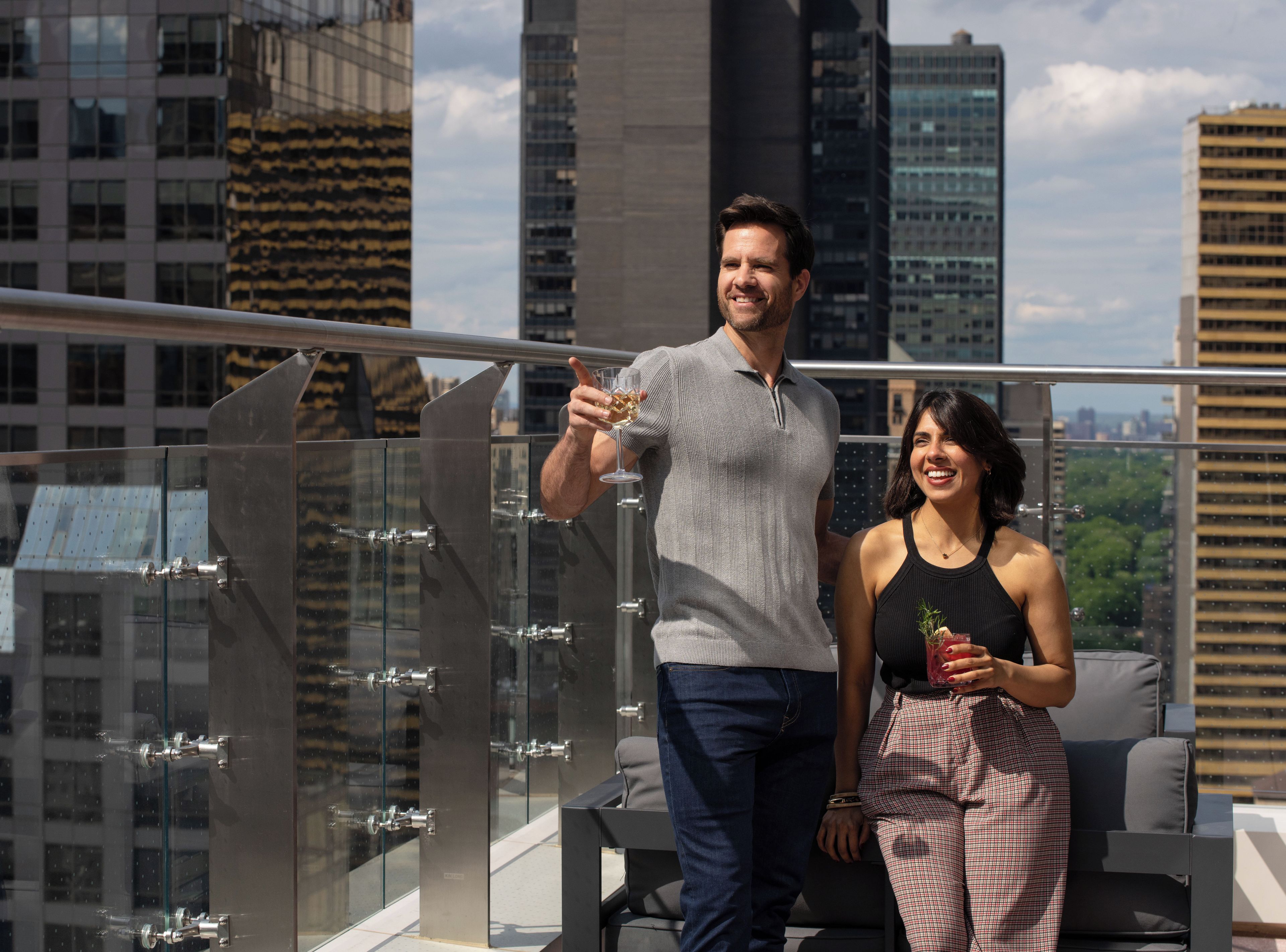 Un homme et une femme sur une terrasse en toit, avec la silhouette de la ville en arrière-plan.