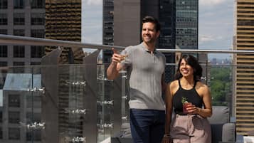 Un homme et une femme sur une terrasse en toit, avec la silhouette de la ville en arrière-plan.