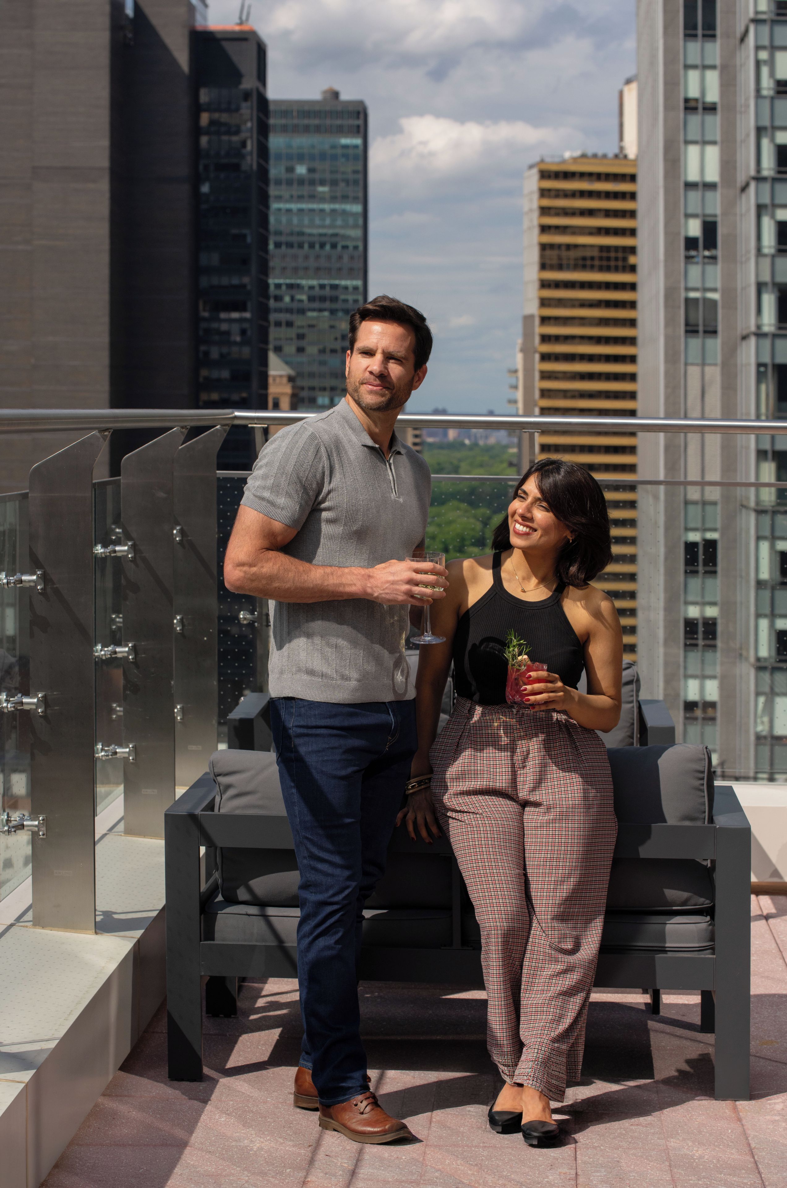 Un homme et une femme se tiennent sur un balcon, avec une vue sur la ville, une balustrade en verre et un bâtiment moderne en arrière-plan.