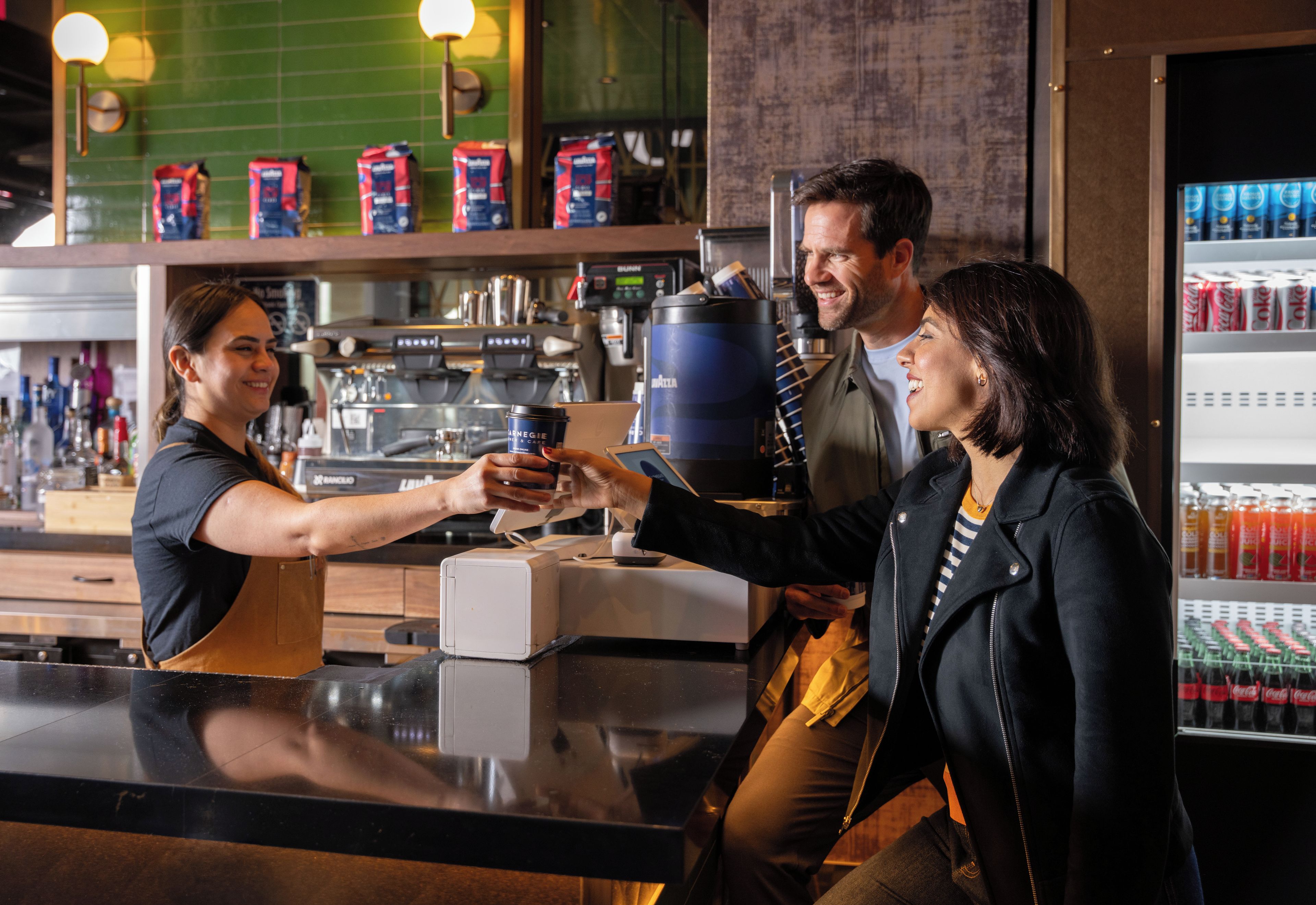 Un barista prepara una bebida en la barra, con una máquina de café y una caja registradora.