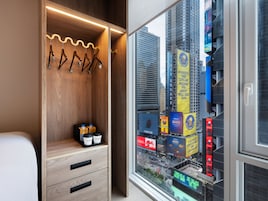 A hotel room with a wooden wardrobe, a window with a city view, and a small table with two containers.