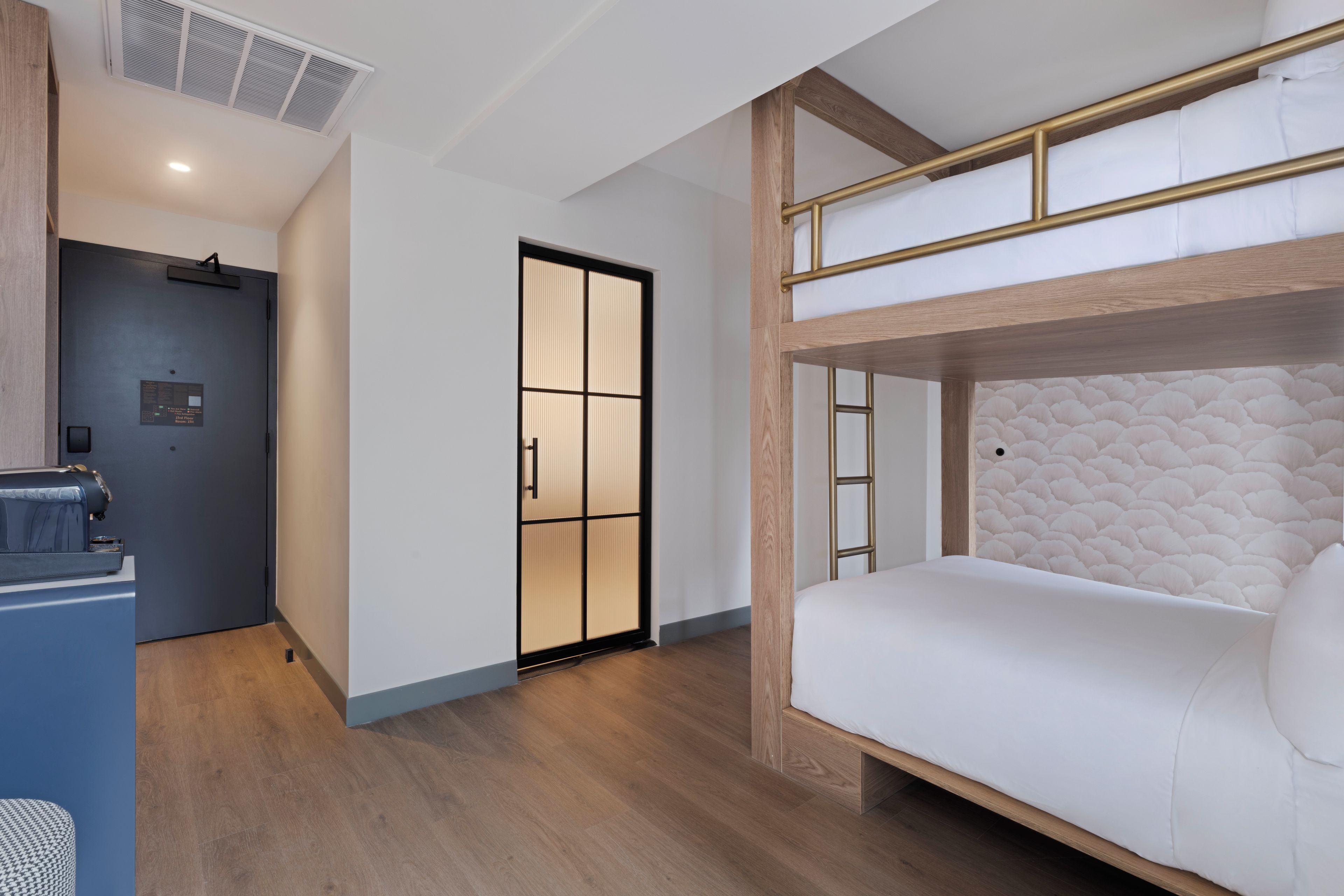 Una habitación de hotel moderna con una cama litera, un escritorio y una puerta corredera que da a otra habitación.