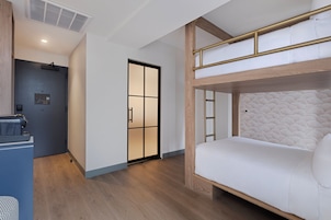 Quarto de hotel moderno com beliche, escrivaninha e porta deslizante que dá para outro espaço.