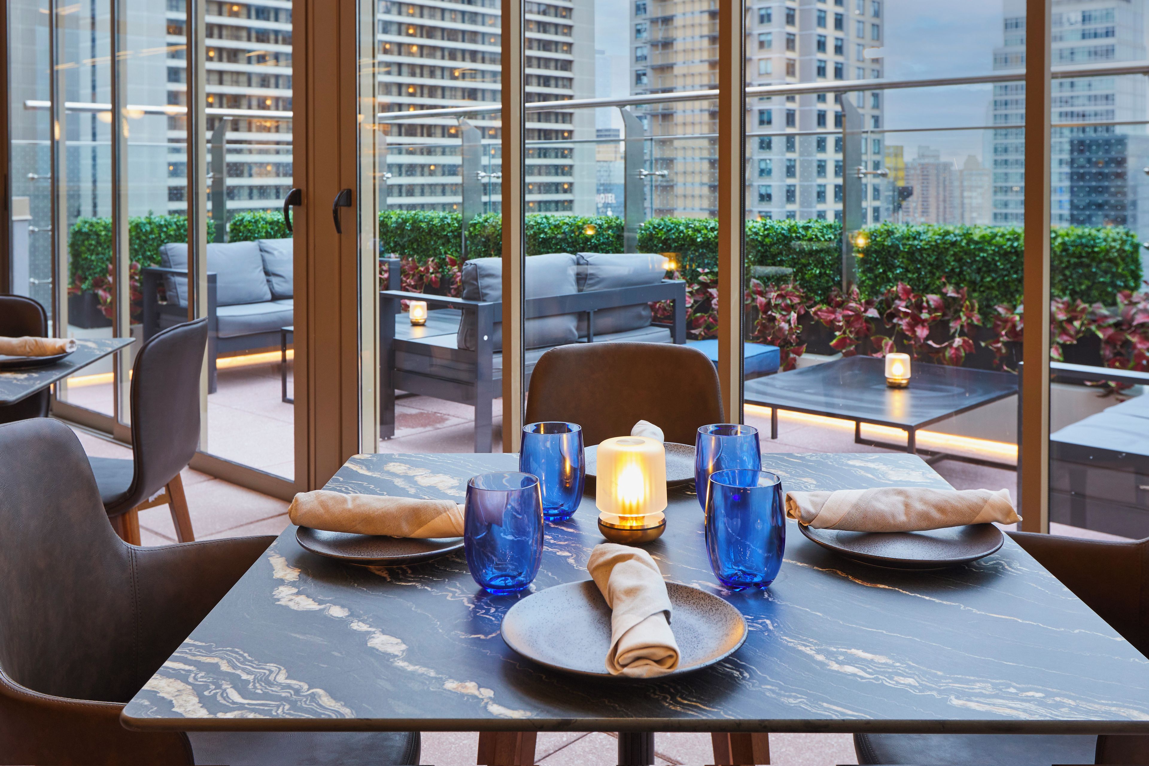 A dining area with tables set for two, featuring a city view through large windows.