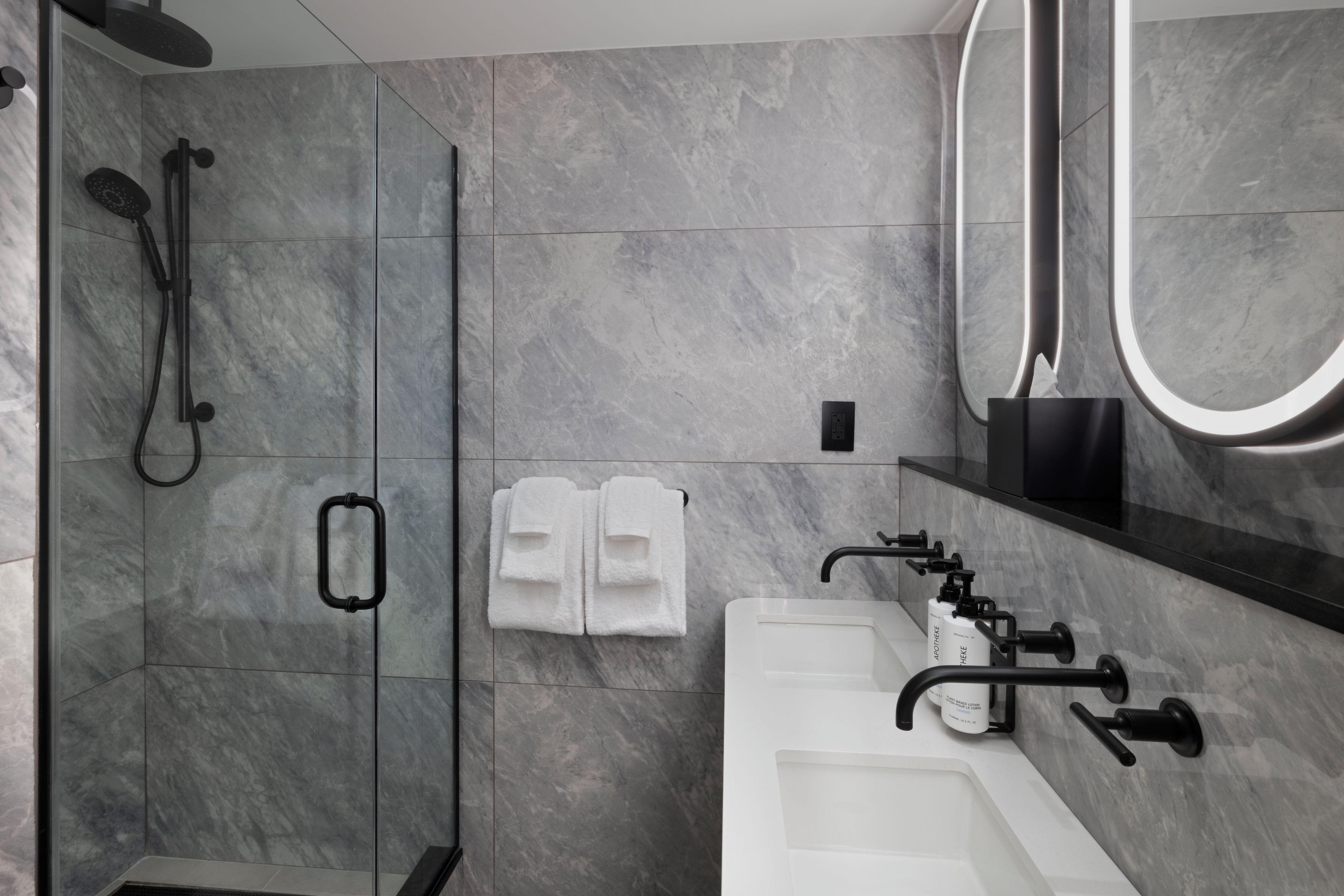 A modern bathroom with a glass-enclosed shower, a white sink with a black faucet, and a black soap dispenser.