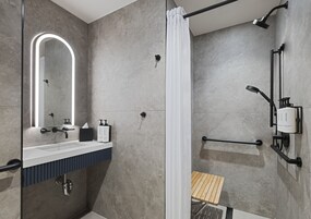 Uma casa de banho moderna com chuveiro, lavatório com espelho e um porta-toalhas.