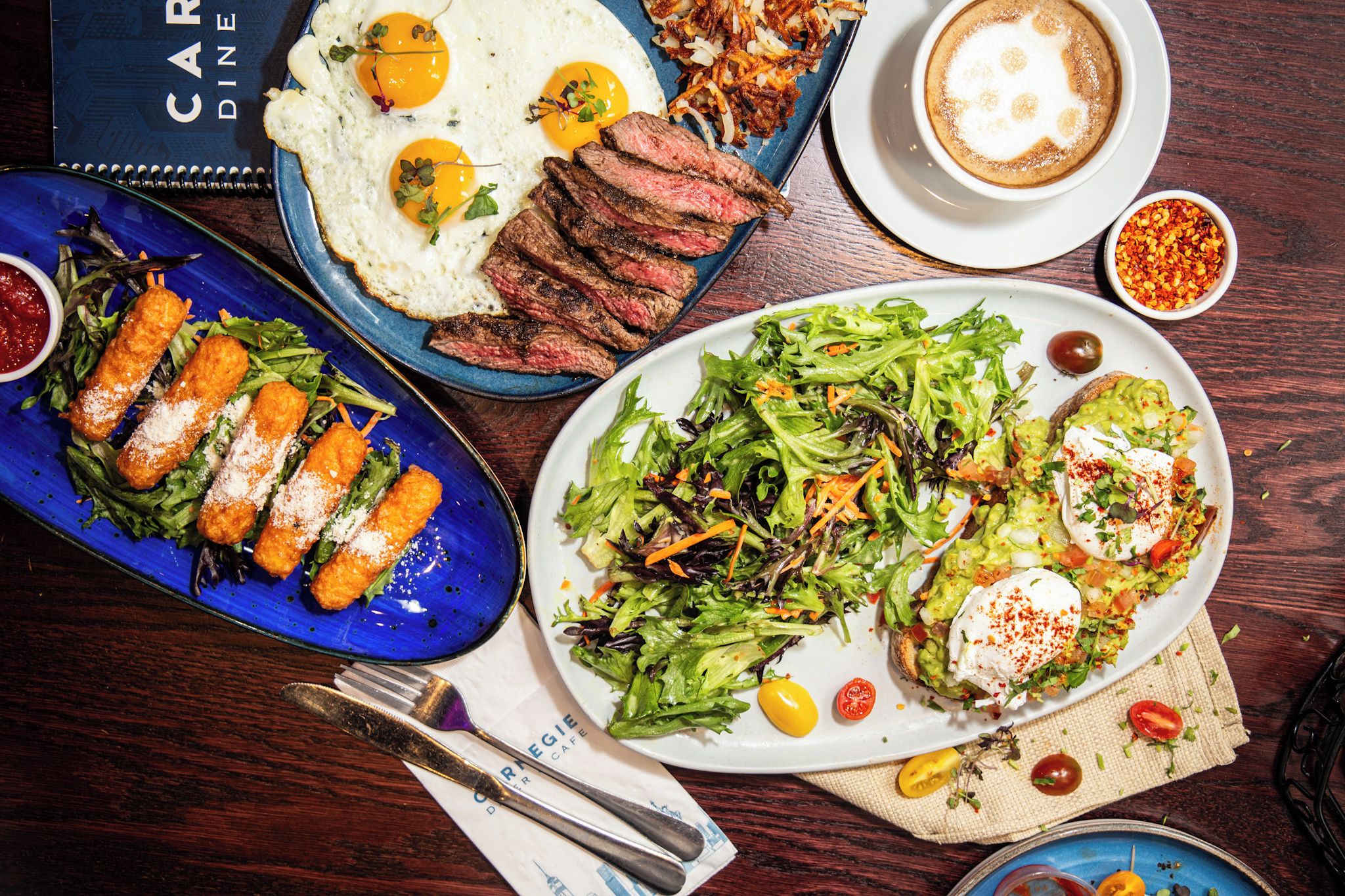 A variety of dishes including steak, eggs, and salads, suggesting a restaurant setting.
