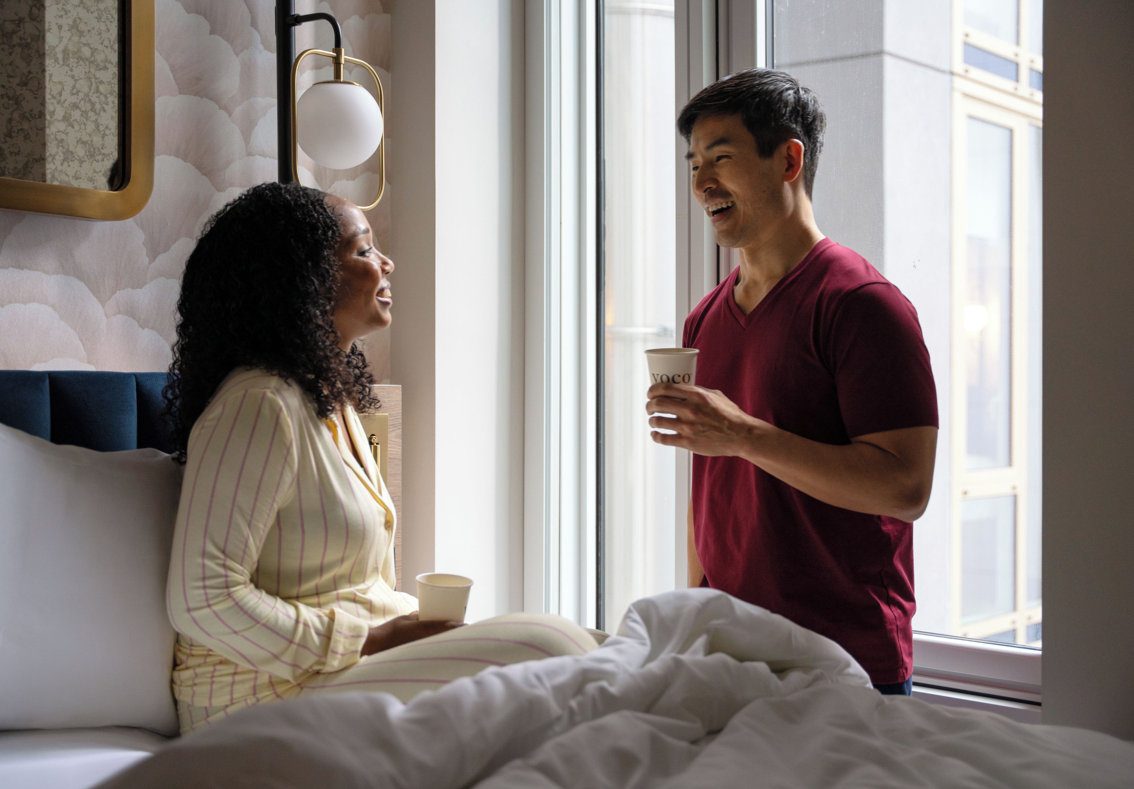 A room with a bed, a window, and a wall-mounted lamp.