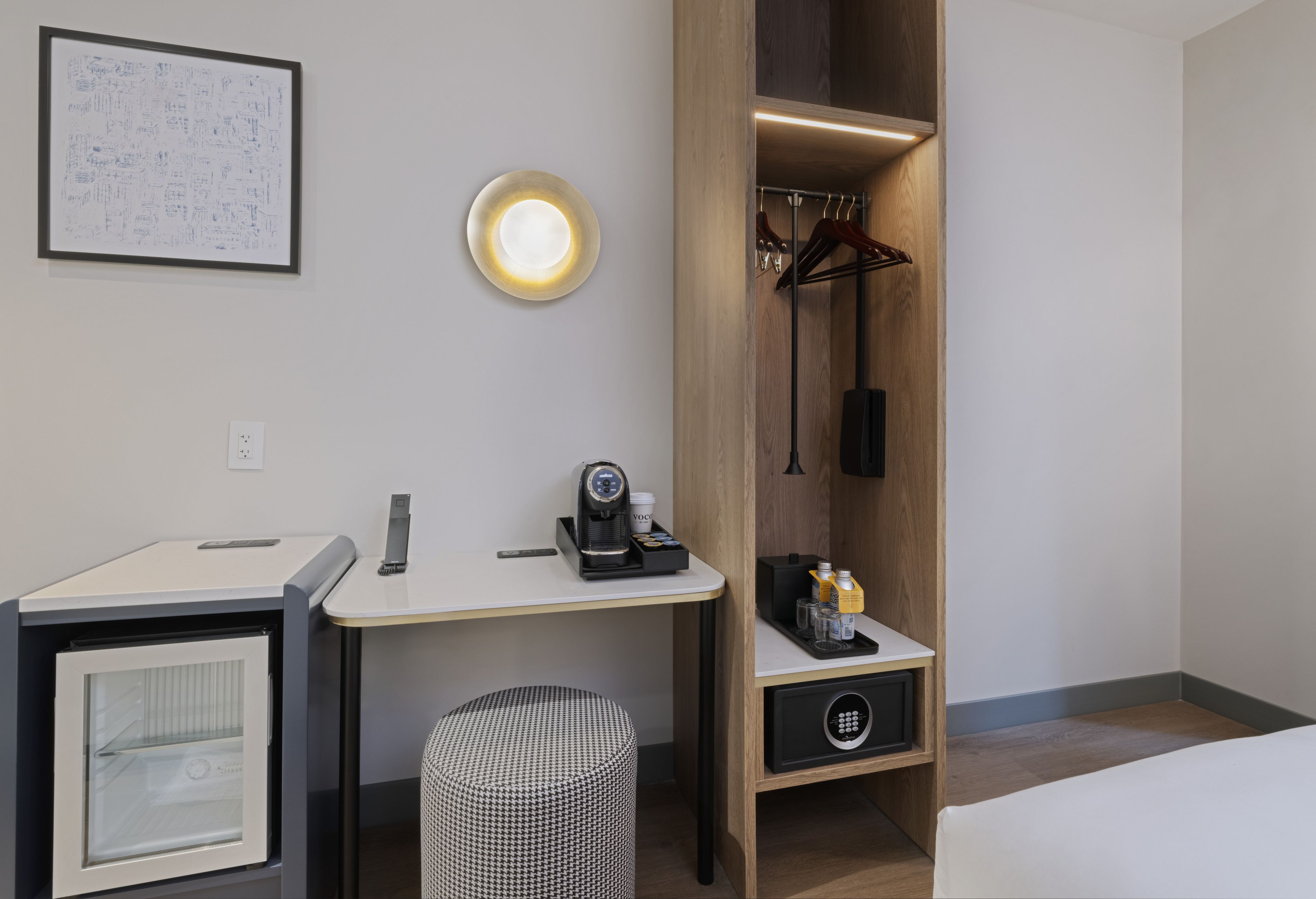 A hotel room with a desk, a coffee machine, a small cabinet, a hanging coat rack, and a bed.