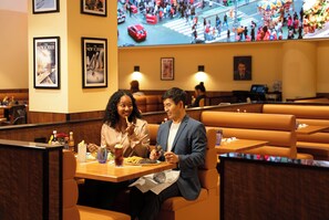 Restaurante com cabines, uma tela de TV exibindo uma rua movimentada e quadros nas paredes.