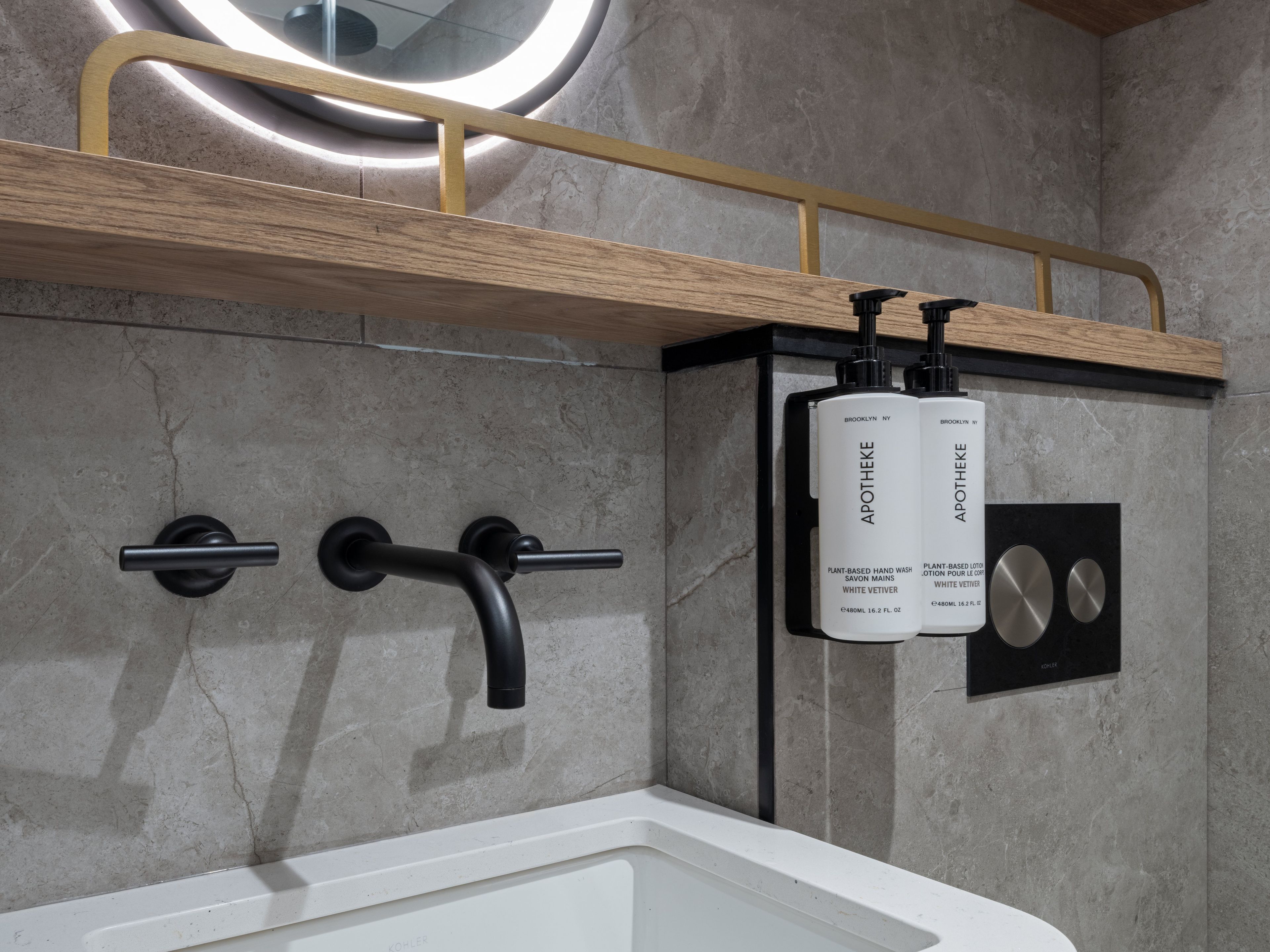Un baño con diseño moderno, que incluye una bañera, un estante de madera con dos botellas de jabón de manos Apotheke y un grifo negro.