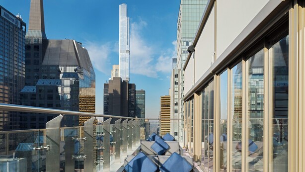 Una terraza moderna en la azotea con barandillas de vidrio, una zona de estar con cojines y vistas al horizonte de la ciudad.