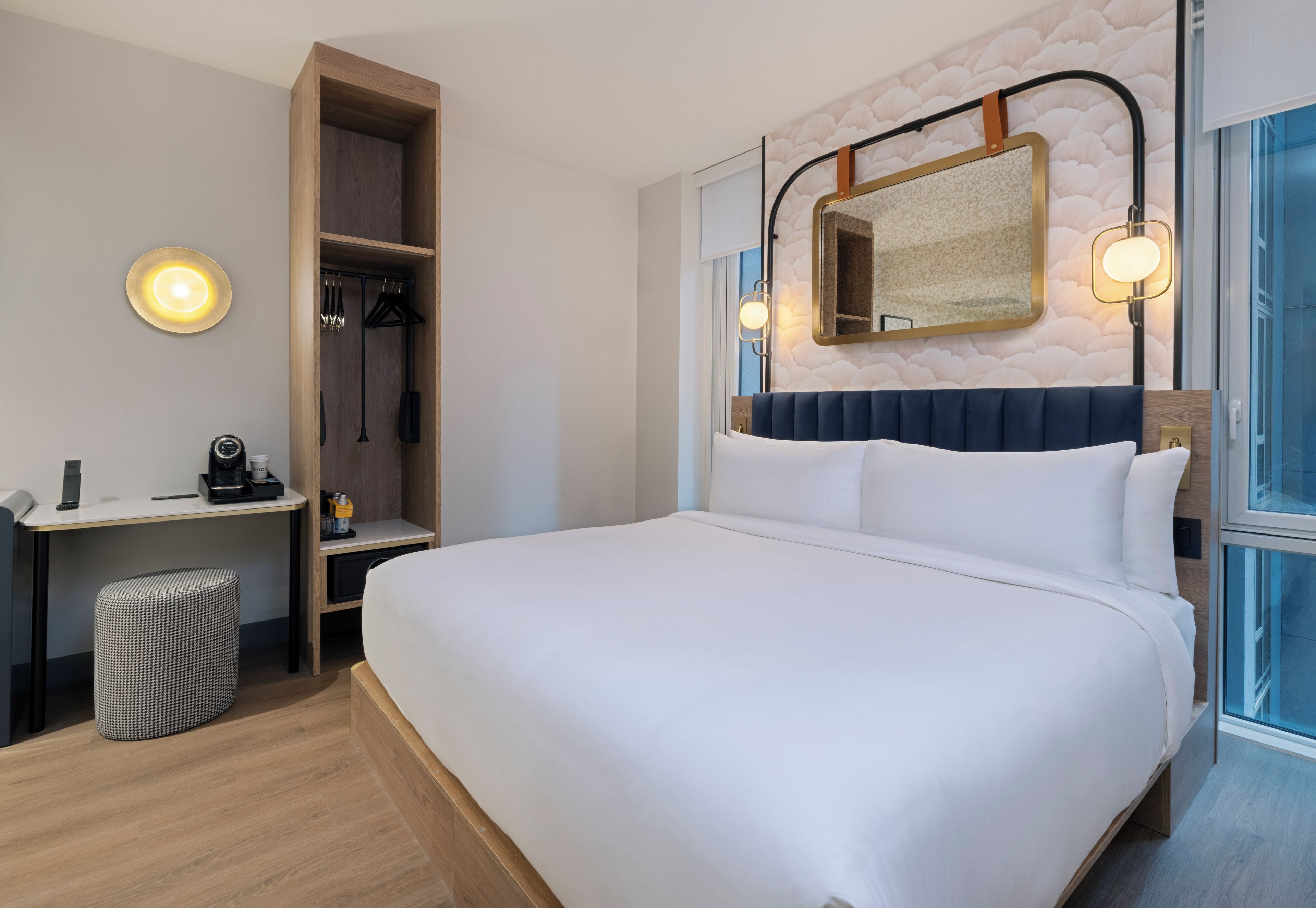 Habitación de hotel con una cama grande, un escritorio con cafetera, armario y baño con espejo.