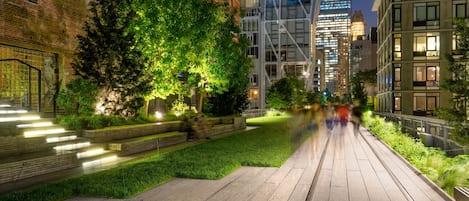 A nighttime urban pathway with modern buildings, a well-lit tree, and a brick wall.