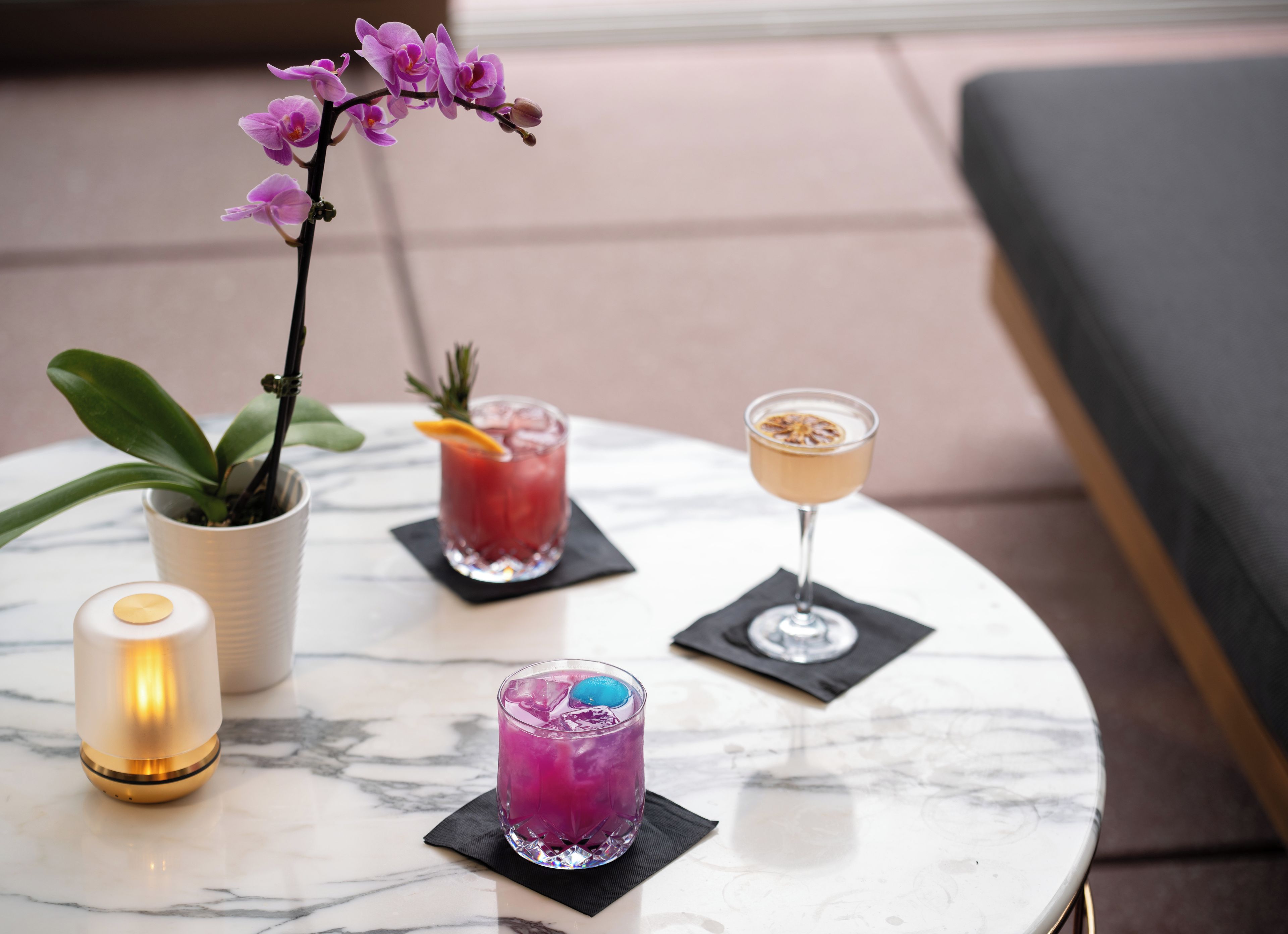 Une table en marbre avec trois boissons, une bougie et une orchidée en pot.