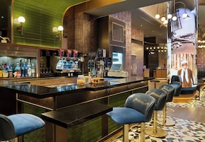 A modern bar area with a counter, bar stools, and a variety of bottles.