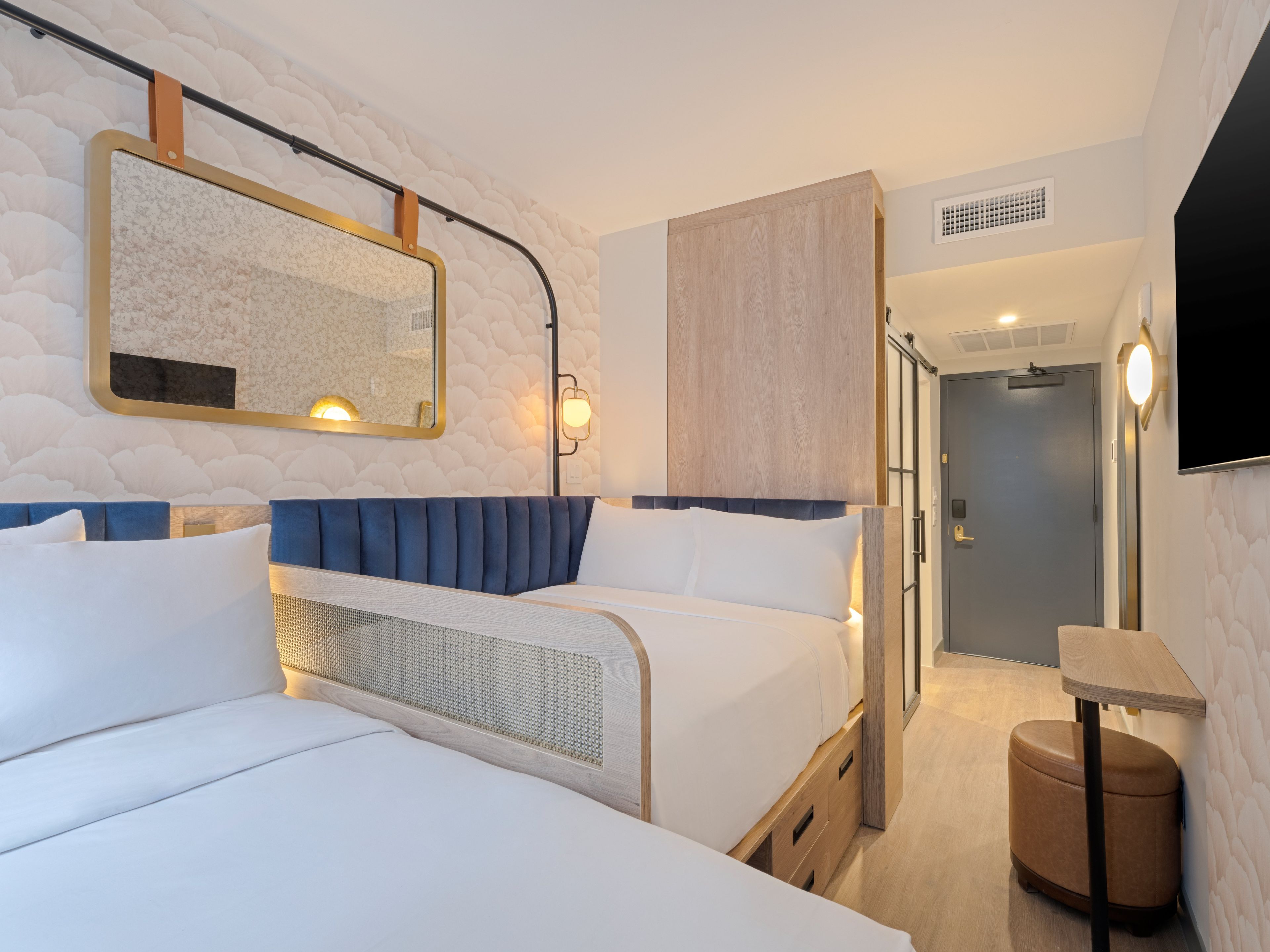 Una habitación de hotel moderna con dos camas, un espejo grande, un armario de madera, una mesita pequeña y un televisor.