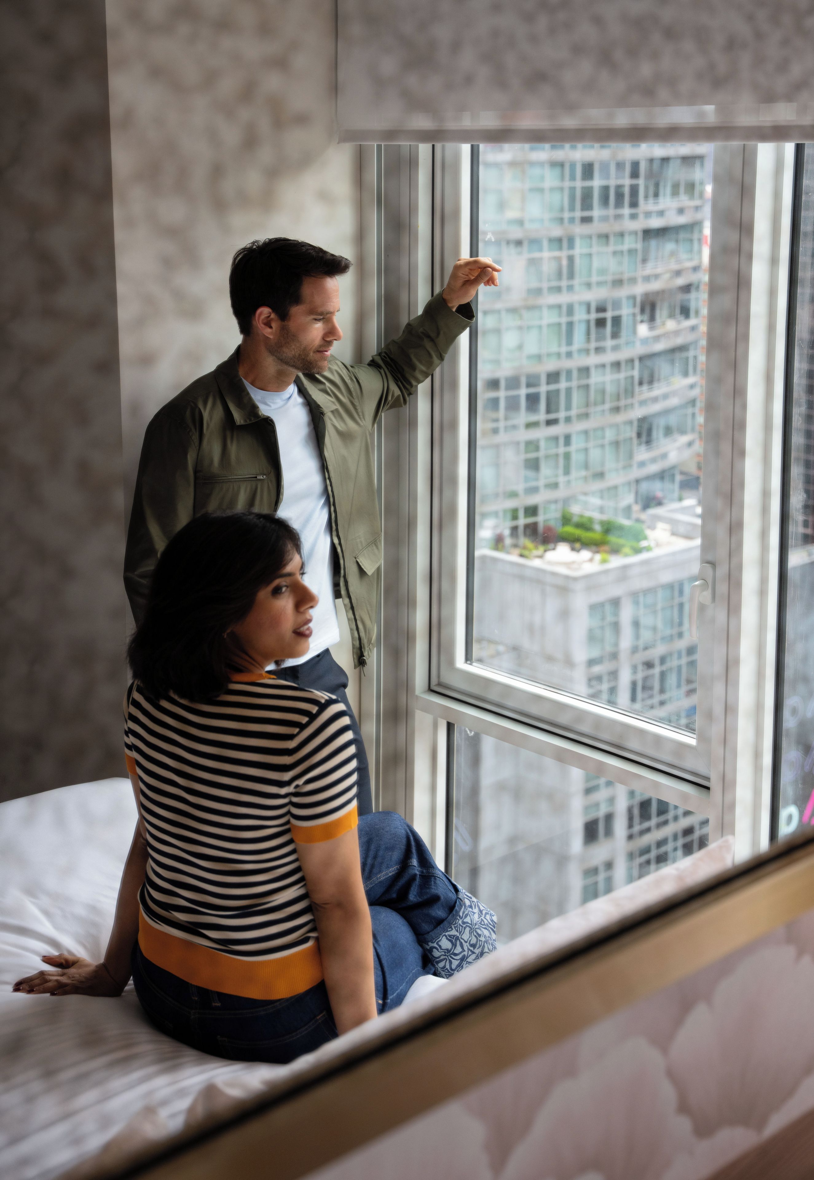 Una persona sentada en una cama mirando por la ventana una vista panorámica de la ciudad.