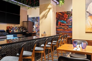 Un espace bar doté d’un long comptoir, de différents types de sièges, notamment des tabourets et des tables, et d’une fresque murale représentant un paysage urbain.