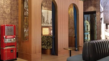 Un hall con paneles de madera, una máquina expendedora roja de estilo vintage y una zona de estar con un sofá estampado.