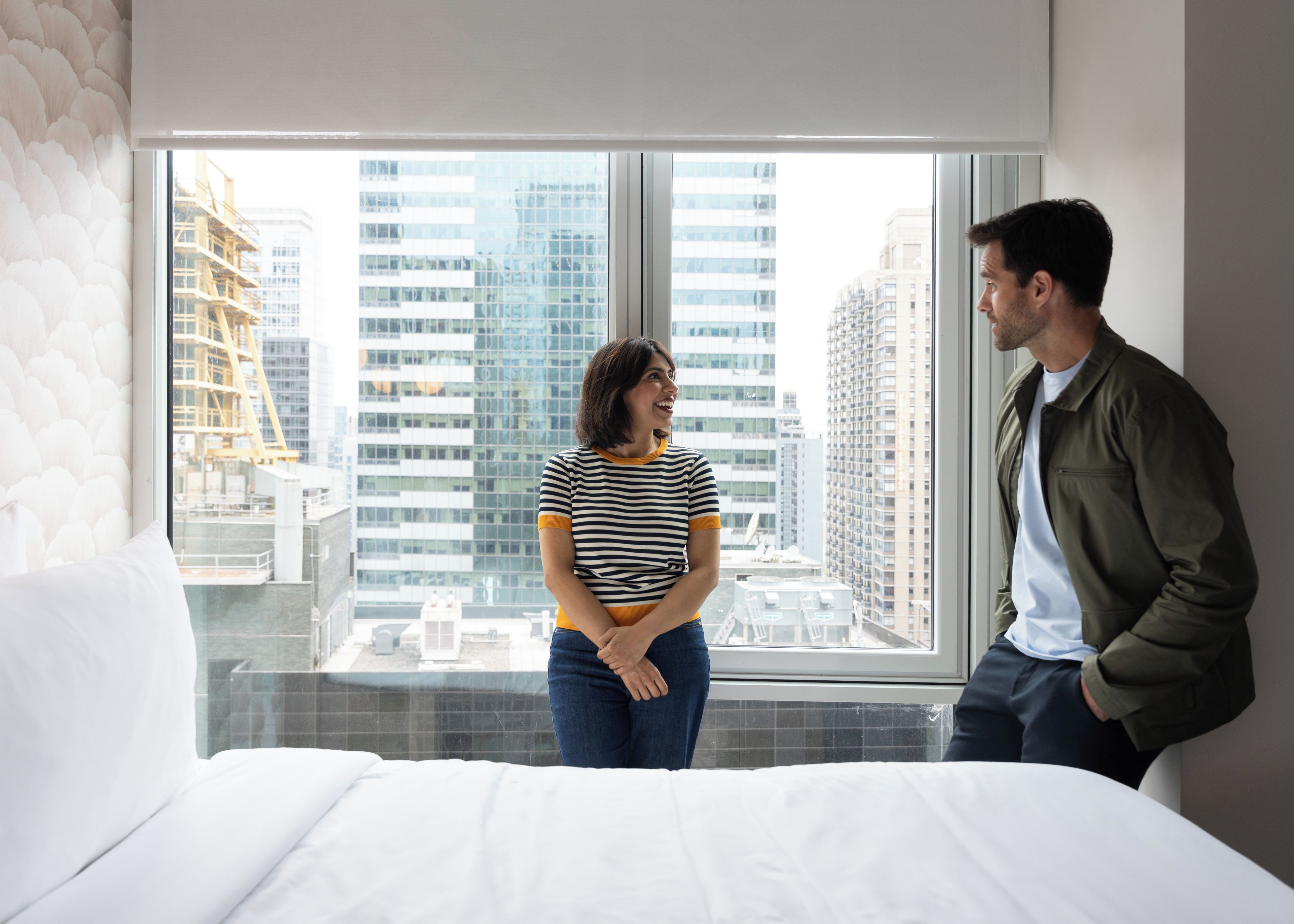 Una habitación de hotel con un ventanal grande, una cama y vistas de edificios de la ciudad.