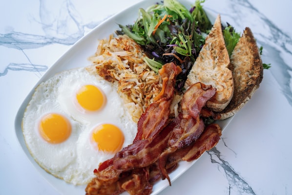 A plate with eggs, bacon, hash browns, toast, and a salad. - voco Times Square - Broadway by IHG (New York)
