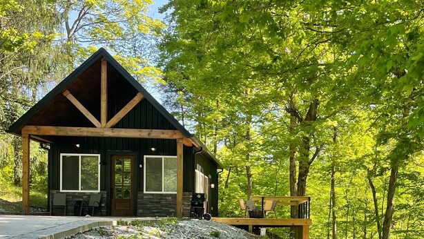 A cabin with a stone foundation, large windows, and a wooden deck. - Nash’s cabin in Leitchfield that is Pet Friendly, WIFI, w/ Creek. (Leitchfield)