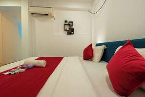 A modern hotel room with a neatly made bed, a red throw blanket, and a small shelf with decorative items. - Morjim Sea Waves (Morjim)
