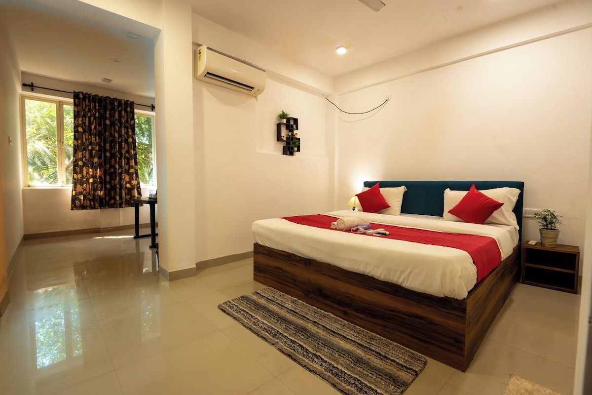 A modern bedroom with a large bed, a bedside table, an air conditioning unit, and a view of the outdoors.
