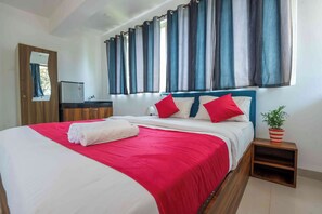 Cama bem arrumada com roupa de cama vermelha e branca, uma pequena mesa de cabeceira com uma planta em vaso e um espelho na parede.