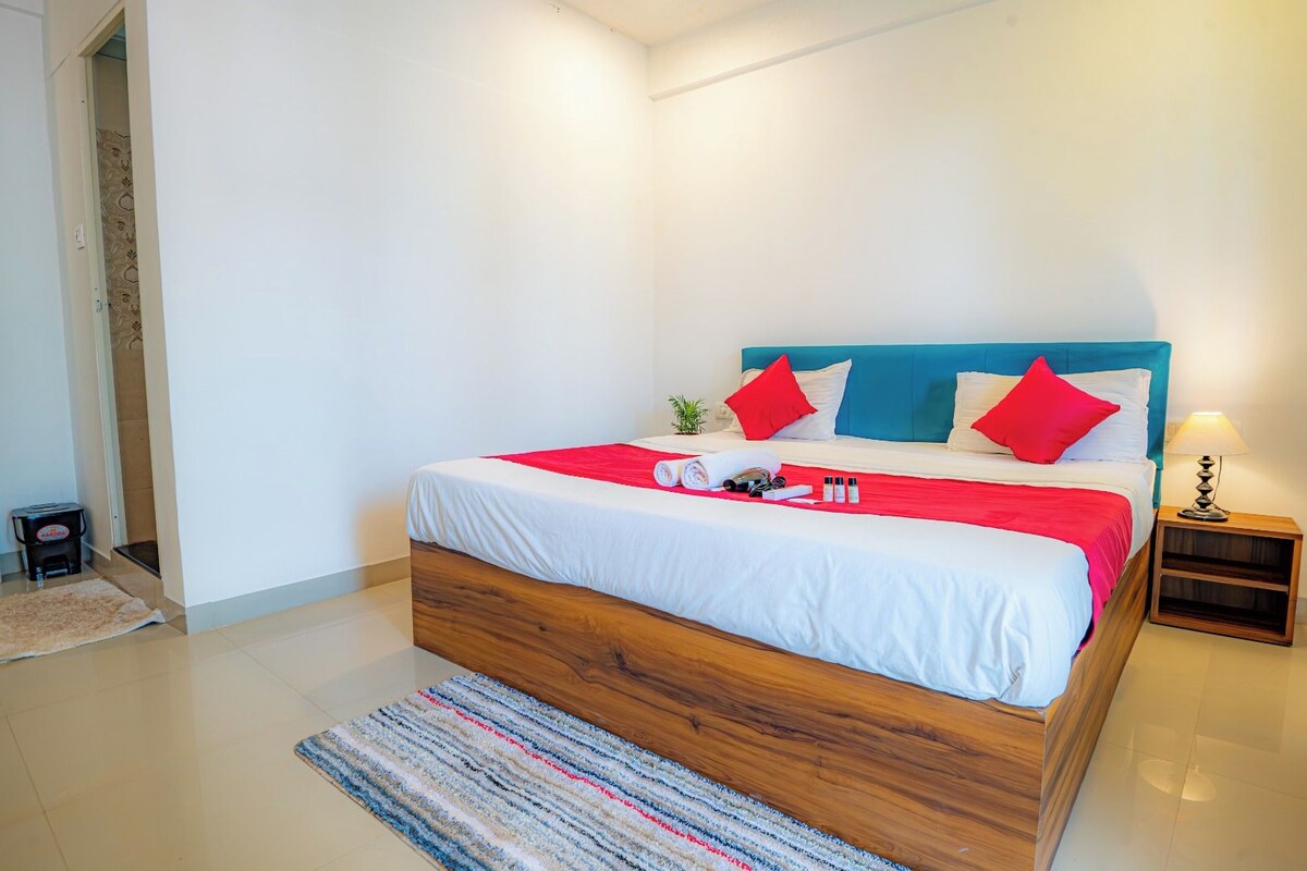 Un dormitorio moderno con estructura de cama de madera, ropa de cama blanca y detalles en rojo.