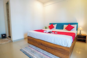 Un dormitorio moderno con estructura de cama de madera, ropa de cama blanca y detalles en rojo.