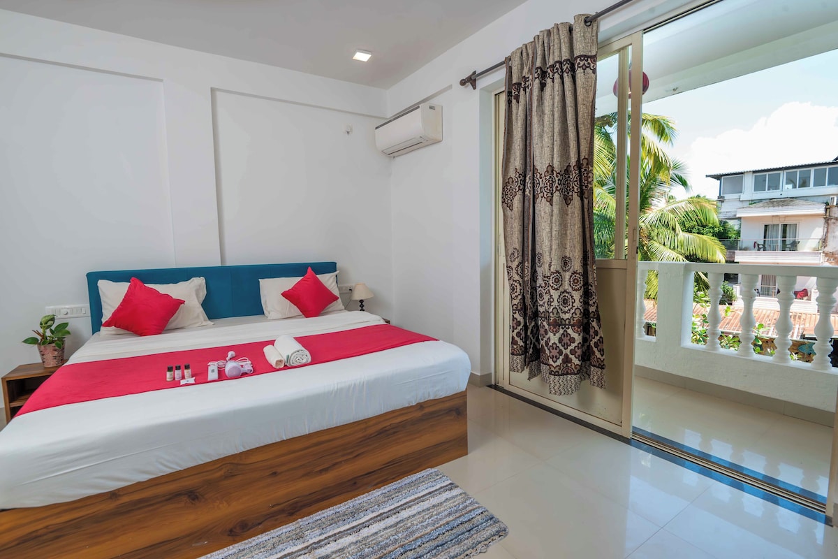 A bedroom with a bed, pillows, a bedside table, a window with curtains, and a view of the outside.