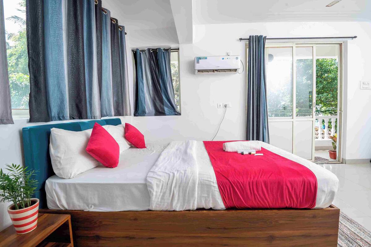 A bedroom with a bed, curtains, an air conditioning unit, and a view of the outdoors.