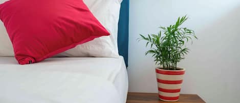 A bed with a red pillow and a striped plant pot on a wooden nightstand.