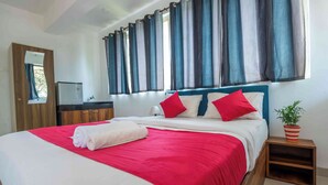 A neatly made bed with a red and white bedspread, a wooden headboard, and two red pillows. There is a small bedside table with a potted plant. - Morjim Sea Waves (Morjim)