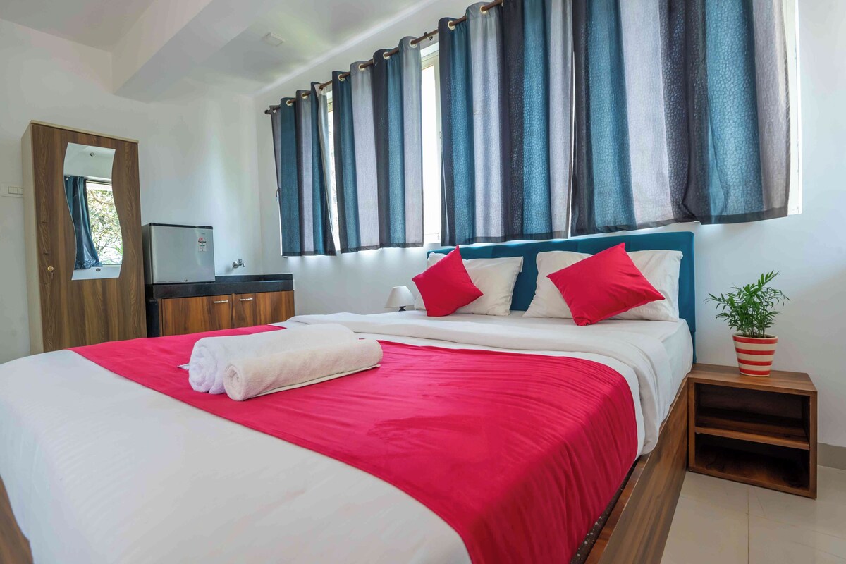 A neatly made bed with a red and white bedspread, a wooden headboard, and two red pillows. There is a small bedside table with a potted plant.