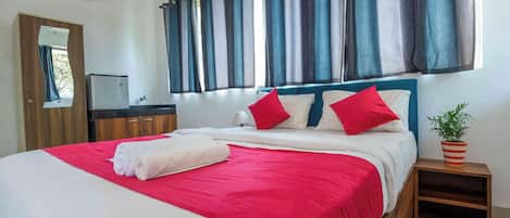 A neatly made bed with a red and white bedspread, a wooden headboard, and two red pillows. There is a small bedside table with a potted plant.