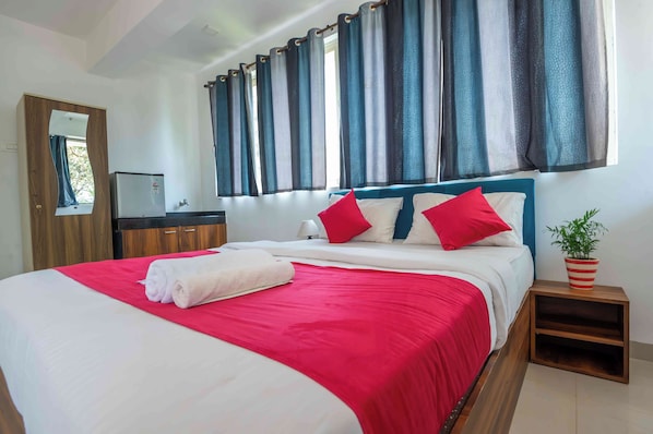 A neatly made bed with a red and white bedspread, a wooden headboard, and two red pillows. There is a small bedside table with a potted plant. - Morjim Sea Waves (Morjim)
